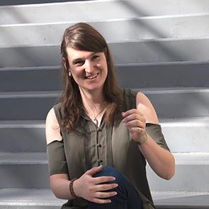 An image of Bronwyn Howell sitting on a flight of stairs and smiling.