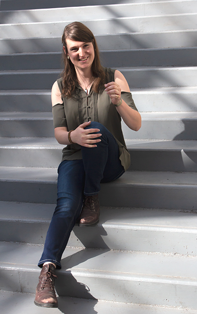 An image of Bronwyn Howell sitting on a flight of stairs and smiling.